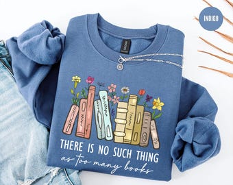 May include: Indigo blue sweatshirt with the text "THERE IS NO SUCH THING as too many books". The graphic features a stack of books with colorful flowers. A silver necklace is draped on the sweatshirt.
