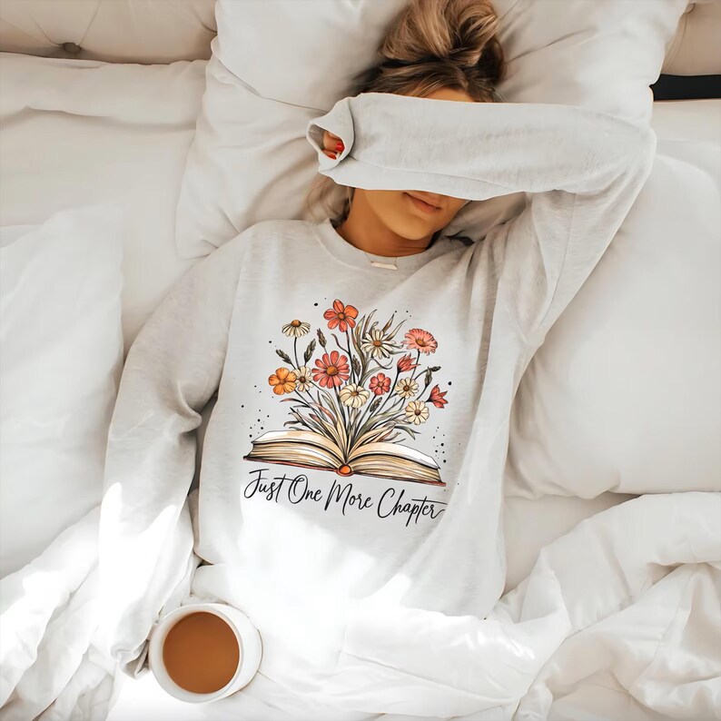 May include: A white sweatshirt with a floral design and the text "Just One More Chapter".