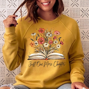 May include: Mustard yellow sweatshirt with a graphic of an open book with flowers on top. The text "Just One More Chapter" is printed below the book.