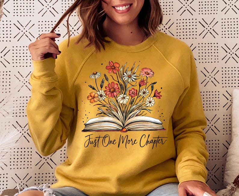 May include: Mustard yellow sweatshirt with a graphic of an open book with flowers on top. The text "Just One More Chapter" is printed below the book.