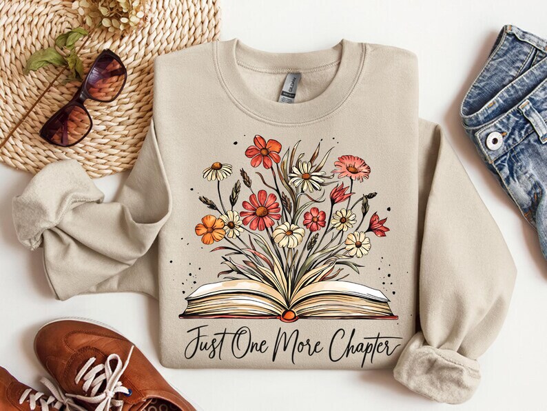 May include: A beige sweatshirt with a floral design and an open book with the text "Just One More Chapter".