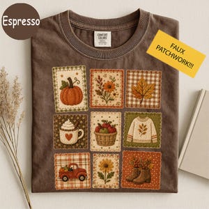 May include: An espresso-colored t-shirt featuring a grid of nine square patches with autumn-themed illustrations, including a pumpkin, flowers, a maple leaf, a mug of cocoa, a basket of apples, a sweater, a red truck, and boots.