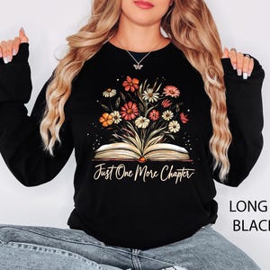 May include: Black long-sleeved sweatshirt with a graphic of an open book with flowers growing out of it. The text "Just One More Chapter" is printed below the book.