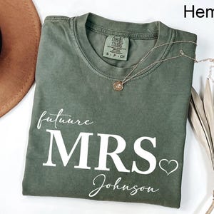 May include: A green hemp t-shirt with the text "future MRS Johnson" in white lettering and a small heart.