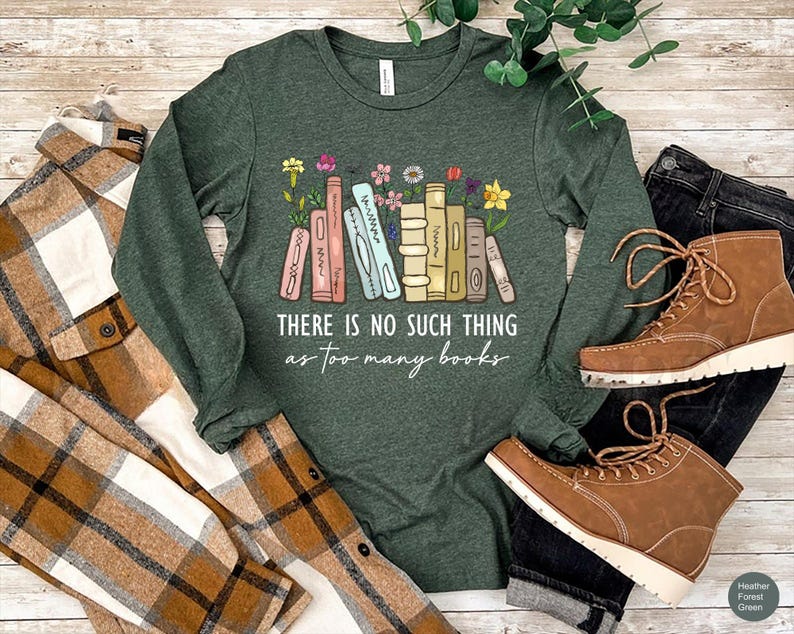 May include: Heather forest green long-sleeve shirt with the text "THERE IS NO SUCH THING as too many books" and a graphic of colorful books and flowers. The shirt is paired with a plaid shirt, black jeans, and brown boots.