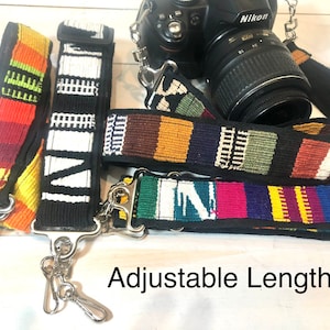 May include: Three colorful camera straps with adjustable length. The straps are woven with different patterns in red, yellow, blue, green, white, and black. The straps are attached to silver metal clasps.