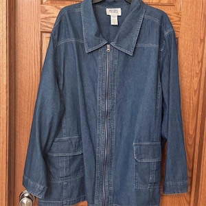May include: A medium-wash blue denim jacket featuring a full-length front zipper, a classic collar, and two large patch pockets with flaps at the lower front. The interior label reads Mainstreet Blues with size information visible.