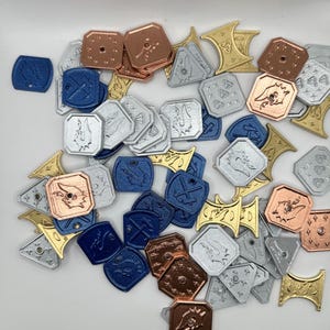 May include: A collection of small, flat, geometric tokens in metallic copper, silver, gold, and blue finishes. The tokens feature various embossed designs, including hammers, dragon heads, and diamond patterns, with some pieces having small holes.