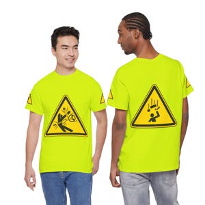 Può includere: Una t-shirt a maniche corte giallo neon con una grafica a triangolo di avvertimento nera e gialla sul davanti e sul retro. La grafica frontale raffigura una persona con un volante, mentre quella sul retro mostra una persona con oggetti in caduta.