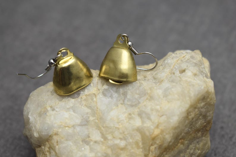 May include: A pair of gold-toned metal bell-shaped earrings featuring a smooth, polished finish. Each earring is attached to a silver-toned metal hook wire, designed for pierced ears, showcasing a simple, functional, and classic bell silhouette.