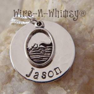 A stainless steel disc customized with your name and a pewter swimming charm sitting on top of disc.
