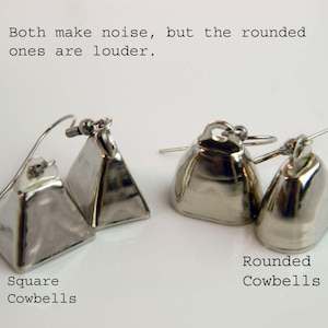 May include: Two pairs of silver-toned metal cowbell earrings with ear wires. The left pair features square-shaped bells, while the right pair features rounded bells. Text on the image reads: Both make noise, but the rounded ones are louder. Square Cowbells. Rounded Cowbells.