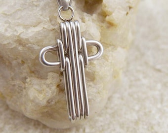 May include: A silver cross pendant with a unique woven design. The cross is made of multiple strands of silver wire that are intertwined to create a three-dimensional effect.