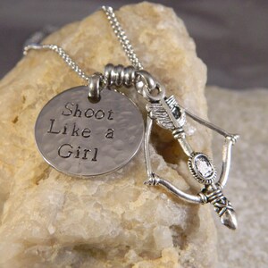 A charm necklace with "Shoot like a girl" on a small disc and your choice of silver or gold tone bow and arrow charm.