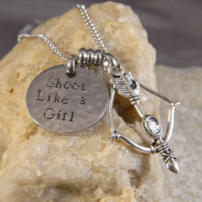 A charm necklace with "Shoot like a girl" on a small disc and your choice of silver or gold tone bow and arrow charm.