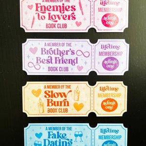 May include: Four colourful book club membership cards with text and illustrations. The cards read "Enemies to Lovers," "Brother's Best Friend," "Slow Burn," and "Fake Dating" book clubs. Each card has a matching "Lifetime Membership" card.