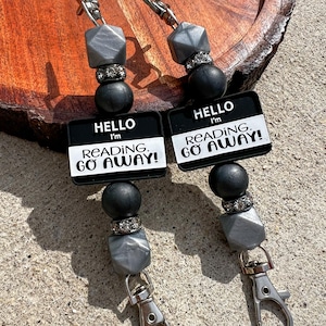 May include: Two beaded badge reels with silver-tone lobster clasps. Each reel has a black, gray, and silver bead design, with a tag that reads "HELLO I'M READING. GO AWAY!" in white text on a black background.
