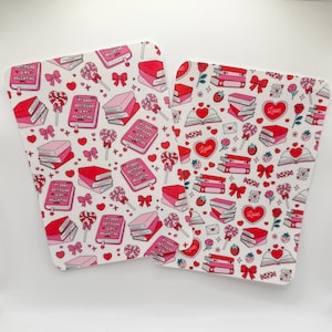 May include: Two white Valentine's Day themed placemats with a repeating pattern of books, hearts, bows, and lollipops in shades of red and pink. One placemat has the text "MY BOOK BOYFRIEND IS MY VALENTINE".