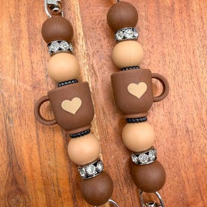 May include: Two beaded lanyards featuring brown and tan silicone spheres, silver-toned rhinestone spacers, and a central brown coffee mug charm with a light tan heart detail. Each lanyard is finished with a silver-colored metal lobster clasp.