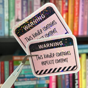 May include: Two pink warning stickers with black text and a holographic finish. The text on the stickers reads "Warning: This kindle contains explicit content".
