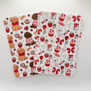May include: White Valentine's Day-themed paper cup sleeves with a repeating pattern of puppies, cupcakes, strawberries, hearts, bows, and candy. The sleeves are designed to fit around a standard coffee cup.