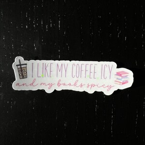 May include: A white sticker with pink and green text that reads "I like my coffee icy and my books spicy". A cartoon drawing of a cup of iced coffee and a stack of books are on either side of the text.