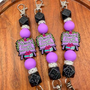 May include: Three keychains with silver clasps, black and silver geometric beads, and purple round beads. Each keychain has a charm with the text "Plot twist: I bought more books" in a green and pink design.