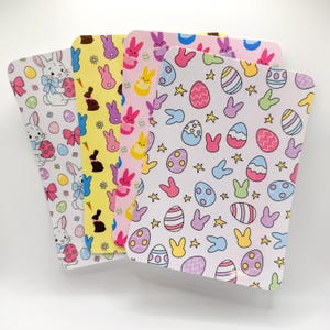 May include: A stack of Easter-themed paper sheets with rounded corners. The sheets feature colorful patterns of bunnies, Easter eggs, bows, and stars in pastel colors. The designs are printed on a white background.