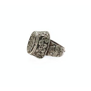 Puede incluir: Un anillo de plata con un diseño intrincado de patrones en espiral. El anillo está hecho de dos piezas, una de las cuales es una pieza redonda y plana con un diseño en relieve.