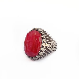 May include: A silver ring with a large, red gemstone set in a detailed, ornate setting.