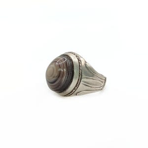 Puede incluir: Un anillo de plata con una piedra de ágata redonda, gris y blanca engastada en el centro. La banda está decorada con un diseño floral.