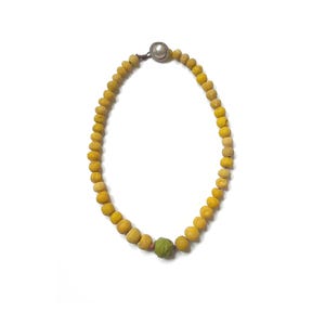 May include: A necklace with yellow beads, a green bead, and a silver clasp. The beads are round and appear to be made of a natural material. The necklace is displayed against a white background.