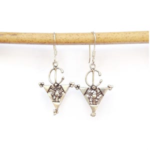 May include: A pair of silver-toned earrings with a triangular design. Each earring features a decorative openwork pattern within the triangle, with a curved element at the top and small embellishments at the bottom. The earrings hang from simple hooks.