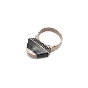 Puede incluir: Anillo de plata con una piedra rectangular a rayas negras y blancas. El anillo tiene una banda sencilla y un engaste cuadrado. La piedra pulida está engastada en un bisel de plata, diseño minimalista.