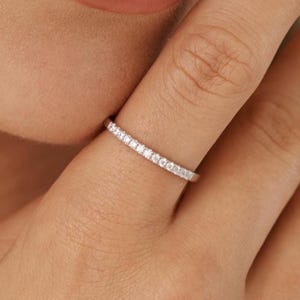 Puede incluir: Un fino anillo de banda de plata con una fila de pequeñas piedras de circonita cúbica transparentes.