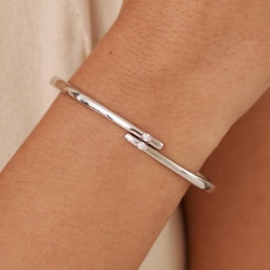 May include: A silver bangle bracelet with two small clear gemstones on the clasp.