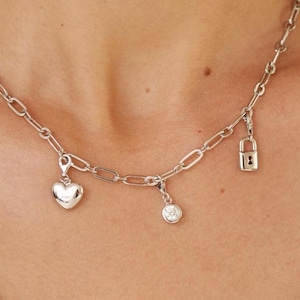 May include: A silver chain necklace with three charms: a heart, a padlock, and a round stone.