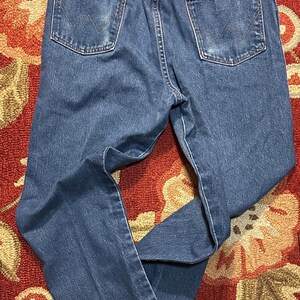 Pode incluir: Cal&ccedil;as de ganga azuis com um design cl&aacute;ssico de cinco bolsos. As cal&ccedil;as de ganga apresentam um corte de perna reto, presilhas para cinto e o log&oacute;tipo Wrangler no bolso traseiro. As cal&ccedil;as de ganga s&atilde;o de lavagem m&eacute;dia e mostram algum desgaste.