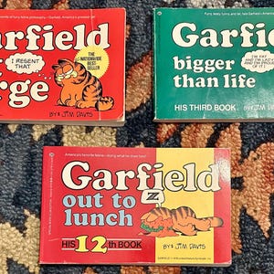 Könnte beinhalten: Drei Garfield-Comicbücher mit roten, grünen und gelben Umschlägen. Die Titel lauten "Garfield at large", "Garfield bigger than life" und "Garfield out to lunch".
