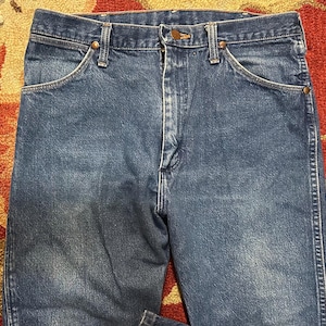 Pode incluir: Close-up de jeans azuis. Os jeans t&ecirc;m um design cl&aacute;ssico de cinco bolsos com fecho de bot&atilde;o e z&iacute;per. O denim tem uma apar&ecirc;ncia desbotada, com desgaste vis&iacute;vel. Os jeans s&atilde;o provavelmente vintage ou usados.