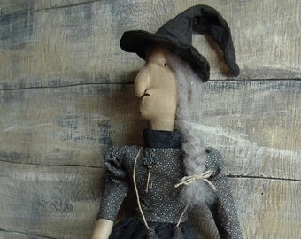 May include: A handmade rag doll witch wearing a black hat, grey hair, and a black and white dress. She is carrying a small black bag with a jack-o'-lantern face.