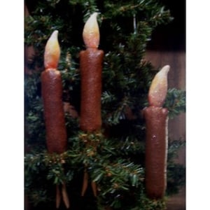 May include: Three brown and white candles with a glittery finish are displayed on a green pine tree branch. The candles are lit and have a warm glow.