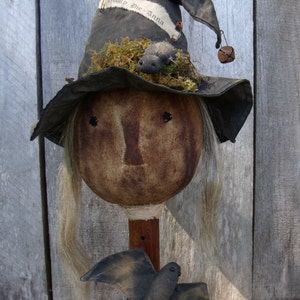 May include: A handmade witch doll with a black hat, a brown face, and white hair. The hat has a white ribbon with the text "Spooky Die Anna" on it. The doll is holding a black bat.