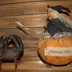 May include: A handmade witch doll riding in a pumpkin carriage pulled by a black cat. The pumpkin has wheels and a sign that reads "Midnight Rider".