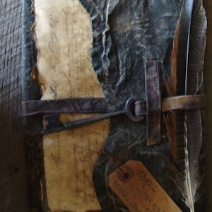Puede incluir: Un diario de cuero azul oscuro con un ojo de cerradura, una pluma y una etiqueta de papel que dice "The Original Journal 1852".