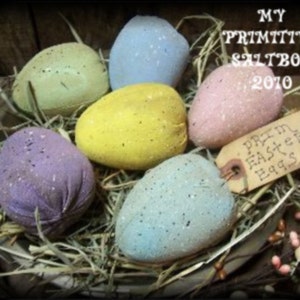Puede incluir: Una colección de seis huevos de Pascua pintados a mano en un nido de paja. Los huevos están pintados en varios colores, incluyendo morado, azul, verde, amarillo y rosa. Los huevos están decorados con un patrón moteado. Un letrero dice "Prim Easter Eggs".
