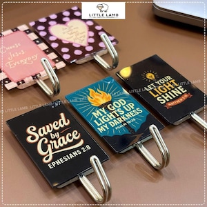 Peut inclure: Cinq patères rectangulaires avec des textes et graphismes religieux. Les motifs incluent 'Choose Jesus Everyday', 'Saved by Grace Ephesians 2:8', 'My God Lights Up My Darkness Psalm 18:28', 'Let Your Light Shine Matthew 5:16' et un motif à pois.