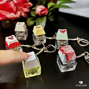 May include: A collection of five mechanical keyboard keycap keychains featuring various designs, including a red polka dot heart, a yellow checkered pattern, a green heart print, a white keycap with the word grace, and a cup graphic with text.
