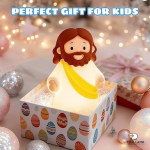 Puede incluir: Una figura luminosa de Jesús, con cabello y barba castaños, vistiendo una túnica blanca y una banda amarilla, se encuentra en una caja decorativa. La caja está adornada con diseños de huevos de Pascua coloridos. El texto "PERFECT GIFT FOR KIDS" está en la parte superior.