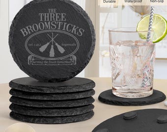 May include: Set of six black slate coasters with a round design. The top coaster features an engraved design of three broomsticks with the text "The Three Broomsticks est 1452 Hogsmeade Serving the finest butterbeer". Each coaster measures 4 inches in diameter and is 0.35 to 0.58 cm thick.